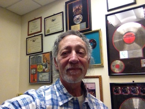 Prof. Bruce Colfin in his office, surrounded by framed gold records and diplomas